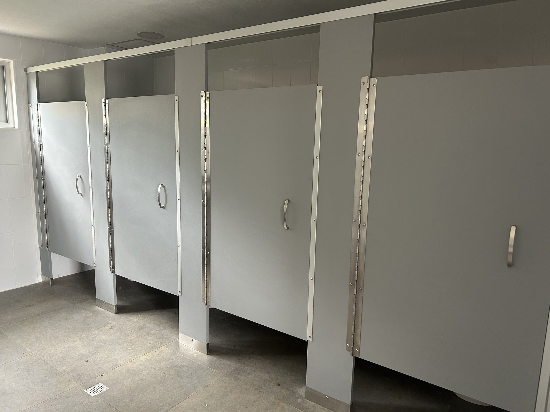 Módulos de baños con particiones grises y bisagras continuas en Edificio Copérnico UAM