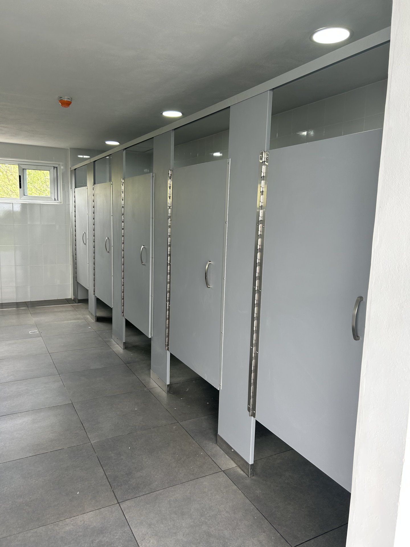 Batería sanitaria universitaria de alto flujo con particiones e iluminación empotrada
