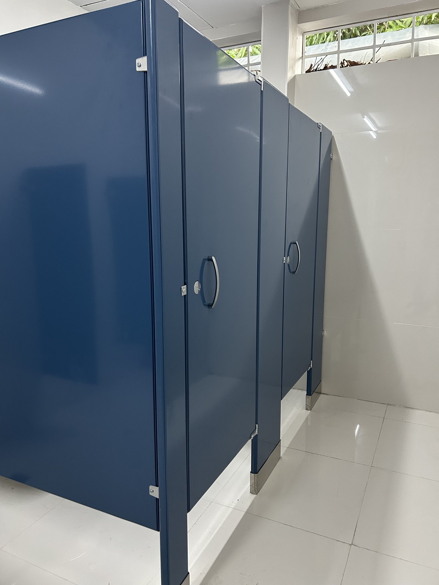 Puertas de cabinas sanitarias con tiradores y zócalos de acero inoxidable en porcelanato pulido